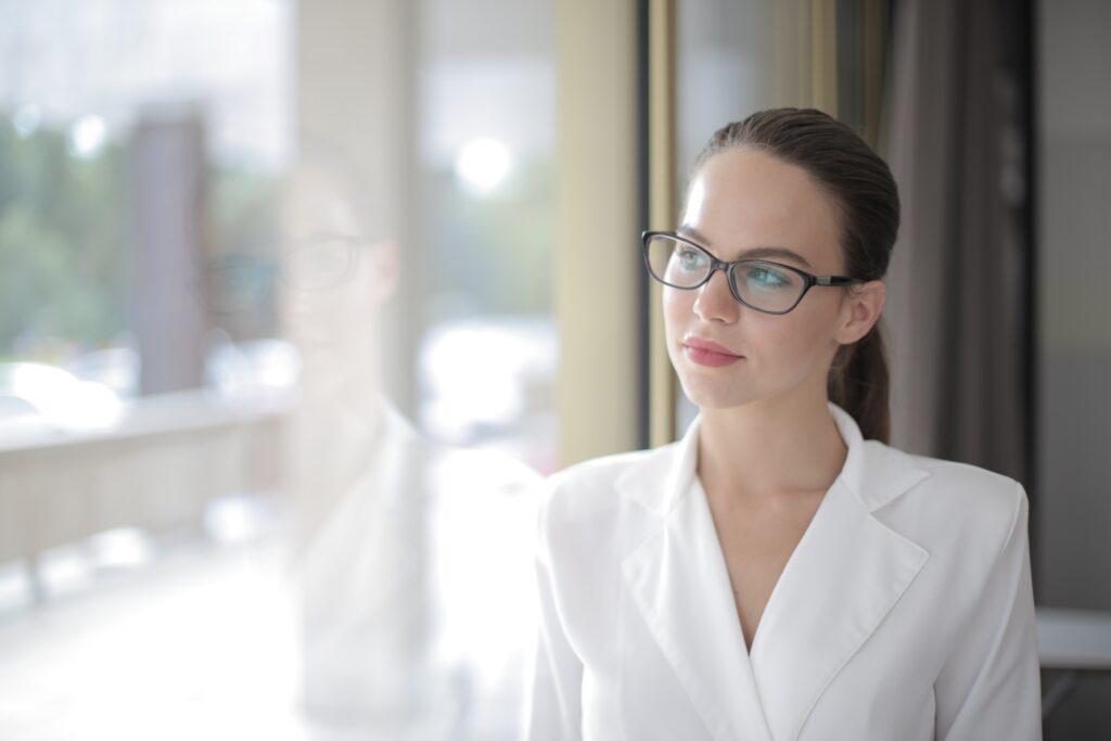 Woman in white shirt and glasses looking out window.